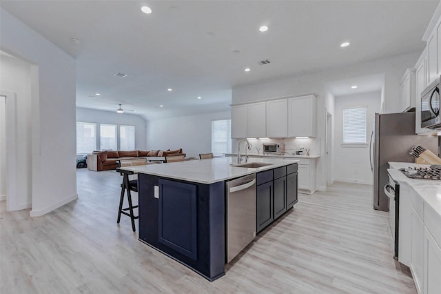 3368 Voda Bend Dr, Katy, TX 77493 - kitchen featuring appliances with stainless steel finishes, light wood finished floors, an island with sink, white cabinetry, and recessed lighting