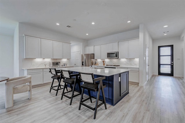 3368 Voda Bend Dr, Katy, TX 77493 - kitchen with appliances with stainless steel finishes, a kitchen island with sink, backsplash, light wood finished floors, and recessed lighting