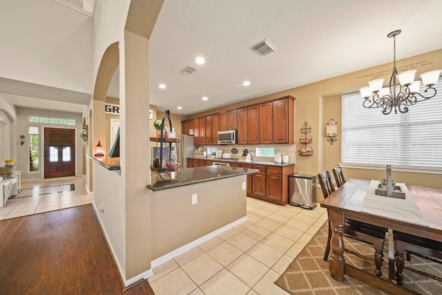 3803 Caleb Ln, Missouri City, TX 77459 - kitchen with stainless steel appliances, arched walkways, light tile patterned floors, a chandelier, and brown cabinets