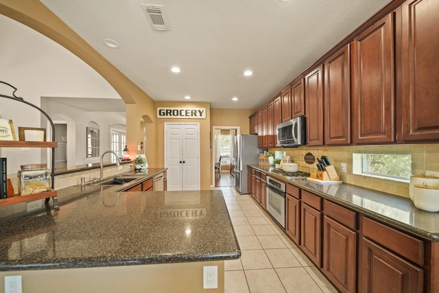 3803 Caleb Ln, Missouri City, TX 77459 - kitchen featuring stainless steel appliances, tasteful backsplash, dark stone counters, light tile patterned floors, and arched walkways