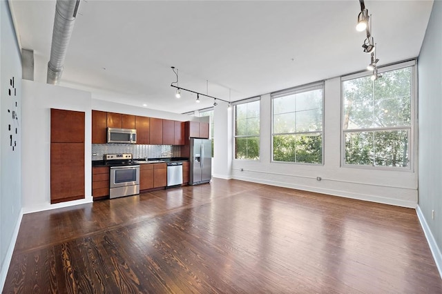 1312 Live Oak St Unit 215, Houston, TX 77003 - kitchen featuring appliances with stainless steel finishes, rail lighting, dark wood-style flooring, decorative backsplash, and dark countertops