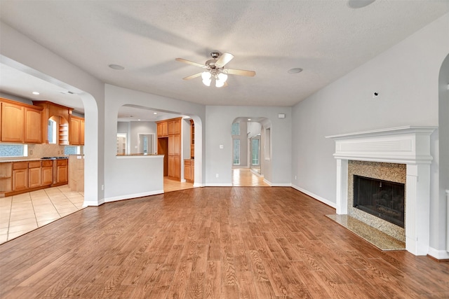 15510 Marble Canyon Way, Houston, TX 77044 - unfurnished living room featuring light wood-style flooring, arched walkways, ceiling fan, a premium fireplace, and a textured ceiling
