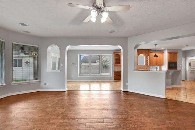 15510 Marble Canyon Way, Houston, TX 77044 - unfurnished living room with arched walkways, light wood-style flooring, a ceiling fan, and a textured ceiling