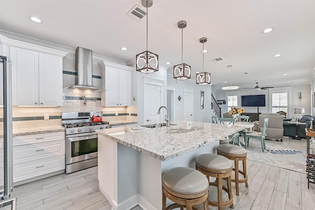 6 Caravelle Ct, Galveston, TX 77554 - kitchen featuring stainless steel gas range, wall chimney exhaust hood, white cabinets, a ceiling fan, and a center island with sink