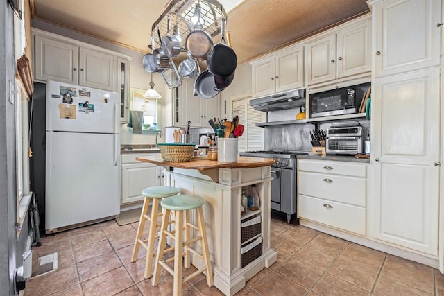 1611 34th St, Galveston, TX 77550 - kitchen featuring stainless steel appliances, under cabinet range hood, wooden counters, white cabinetry, and a center island