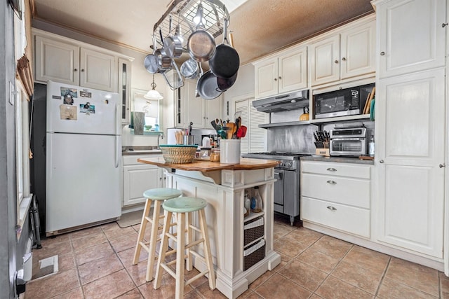 1611 34th St, Galveston, TX 77550 - kitchen featuring stainless steel appliances, under cabinet range hood, white cabinetry, wooden counters, and a center island