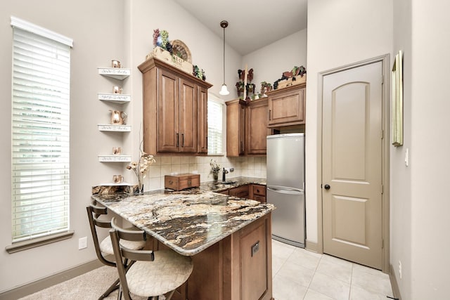13810 Lake Prt, Cypress, TX 77429 - kitchen with freestanding refrigerator, a peninsula, dark stone counters, a breakfast bar area, and tasteful backsplash