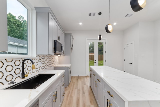 6715 England St, Houston, TX 77021 - kitchen with gray cabinetry, stainless steel microwave, a center island, light wood finished floors, and backsplash