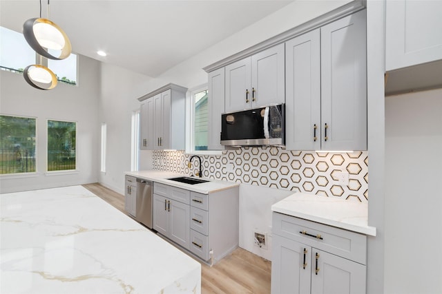 6715 England St, Houston, TX 77021 - kitchen with stainless steel appliances, light stone counters, light wood-type flooring, decorative backsplash, and gray cabinets