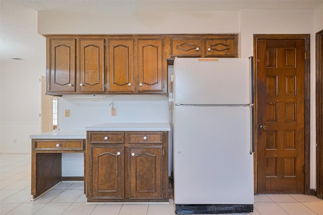 2823 W Pebble Beach Dr, Missouri City, TX 77459 - kitchen with freestanding refrigerator, light countertops, light tile patterned floors, and brown cabinetry