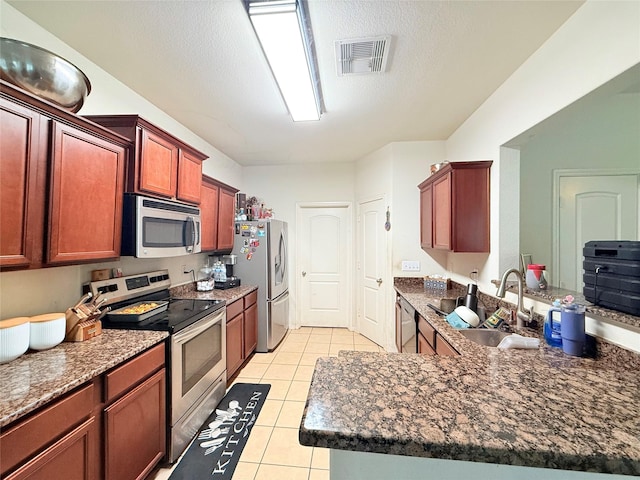 9458 Grand Spark Dr, Rosharon, TX 77583 - kitchen featuring stainless steel appliances, light tile patterned flooring, a peninsula, dark brown cabinets, and dark stone counters