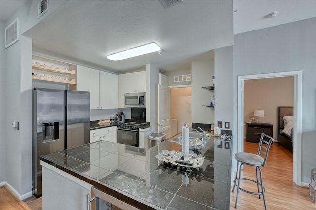 3505 Sage Rd Unit 1206, Houston, TX 77056 - kitchen featuring appliances with stainless steel finishes, light wood-style flooring, white cabinets, a peninsula, and open shelves