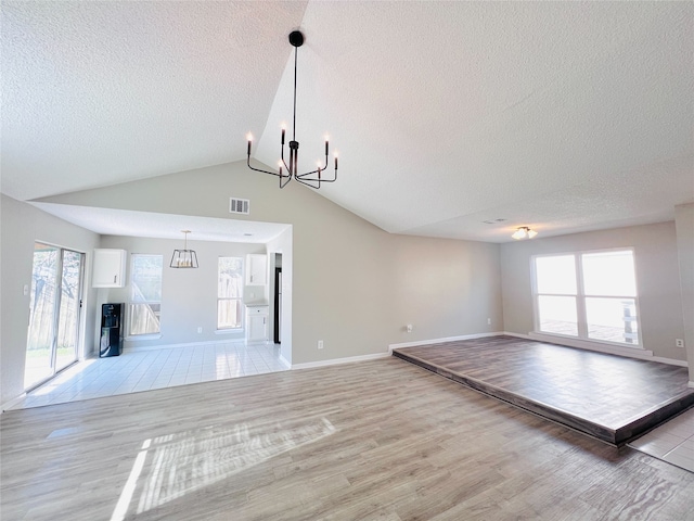 6822 Stonewater, Houston, TX 77084 - unfurnished living room with a chandelier, a textured ceiling, light wood-style flooring, plenty of natural light, and vaulted ceiling