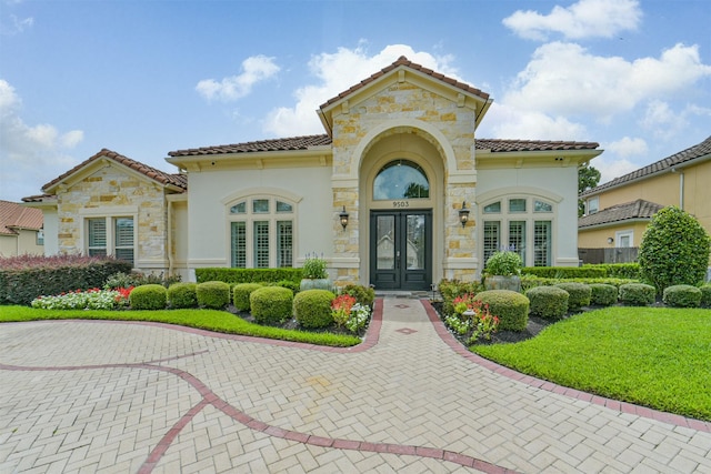 9503 Martha Springs Dr, Houston, TX 77070 - property entrance featuring french doors, stone siding, a tiled roof, stucco siding, and a lawn