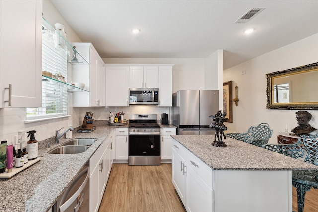 23502 Glenbuck St, Spring, TX 77373 - kitchen featuring stainless steel appliances, light wood-type flooring, a center island, white cabinetry, and light stone counters