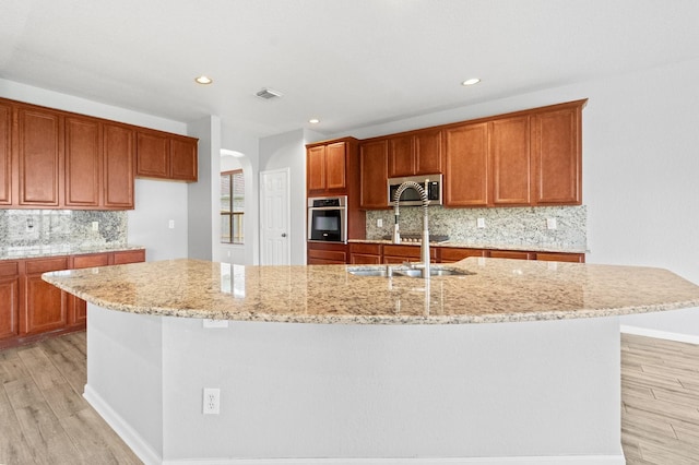 18203 Park Sage Ct, Cypress, TX 77433 - kitchen with stainless steel appliances, light wood finished floors, tasteful backsplash, light stone countertops, and a large island