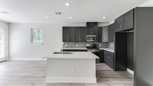 6902 Apollo St, Houston, TX 77091 - kitchen with stainless steel appliances, tasteful backsplash, light wood-style flooring, a center island with sink, and recessed lighting