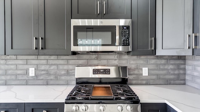 6902 Apollo St, Houston, TX 77091 - kitchen featuring stainless steel appliances, decorative backsplash, light stone countertops, and gray cabinets