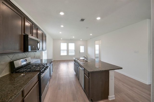 4918 Eldorado Rose Pl, Katy, TX 77493 - kitchen featuring stainless steel appliances, light wood-style floors, dark brown cabinetry, dark stone countertops, and an island with sink