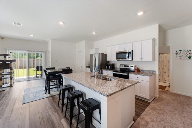 10138 California Lily Ln, Houston, TX 77016 - kitchen with stainless steel appliances, a kitchen island with sink, a breakfast bar area, white cabinets, and recessed lighting
