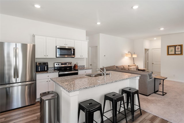 10138 California Lily Ln, Houston, TX 77016 - kitchen featuring appliances with stainless steel finishes, open floor plan, an island with sink, white cabinetry, and a breakfast bar
