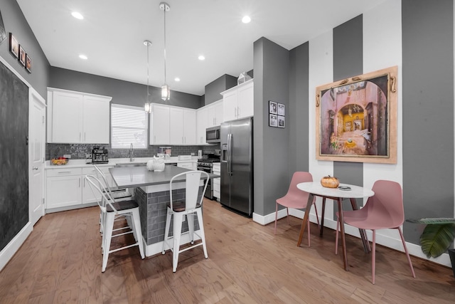 734 W Donovan St, Houston, TX 77091 - kitchen featuring stainless steel appliances, a kitchen island, light wood finished floors, tasteful backsplash, and white cabinets