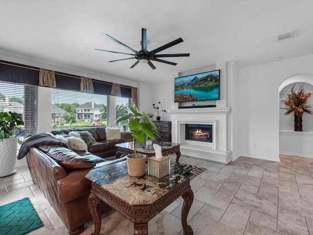11938 Galentine Pt, Cypress, TX 77429 - living area with crown molding, ceiling fan, a lit fireplace, stone tile flooring, and arched walkways