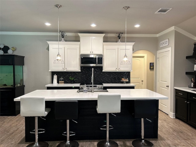 23918 Overcup Dr, Spring, TX 77389 - kitchen featuring stainless steel microwave, arched walkways, a kitchen island with sink, tasteful backsplash, and light countertops