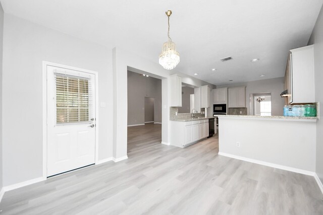 6803 Chapelfield Ln, Houston, TX 77049 - kitchen with light wood finished floors, black microwave, decorative light fixtures, white cabinetry, and backsplash