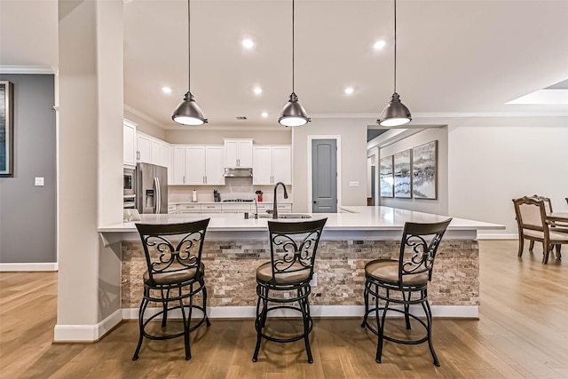 1939 Heather Canyon Dr, Pearland, TX 77089 - kitchen with appliances with stainless steel finishes, under cabinet range hood, white cabinets, ornamental molding, and light countertops