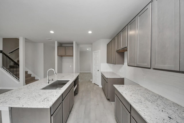 15819 Walnut Leaf Ln, Cypress, TX 77429 - kitchen featuring light stone countertops, backsplash, light wood-style floors, an island with sink, and recessed lighting