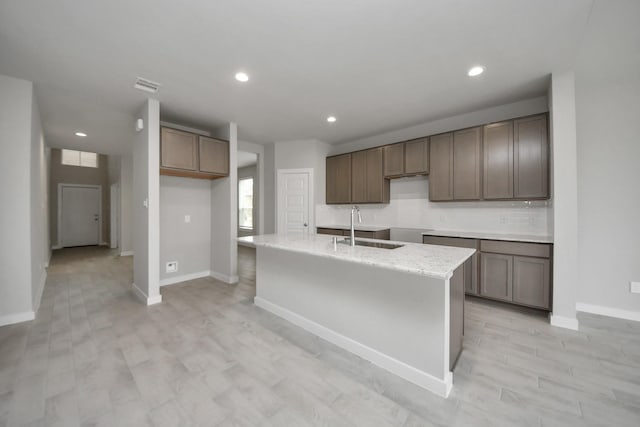 15819 Walnut Leaf Ln, Cypress, TX 77429 - kitchen featuring a kitchen island with sink, recessed lighting, decorative backsplash, light wood-type flooring, and light stone countertops