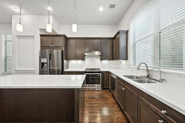 4106 Schuler St, Houston, TX 77007 - kitchen featuring stainless steel appliances, under cabinet range hood, dark brown cabinetry, backsplash, and dark wood-style floors