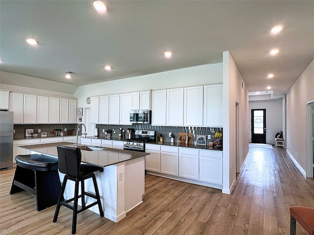 19022 Palizzi Ridge Ln, New Caney, TX 77357 - kitchen with appliances with stainless steel finishes, decorative backsplash, a kitchen island with sink, white cabinetry, and a breakfast bar