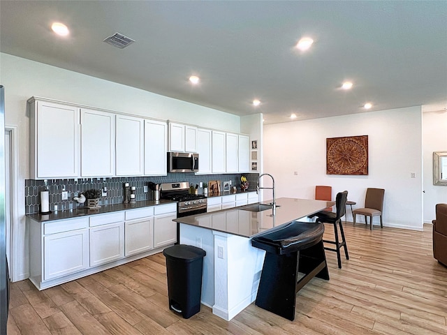 19022 Palizzi Ridge Ln, New Caney, TX 77357 - kitchen with stainless steel appliances, light wood-style floors, tasteful backsplash, dark countertops, and a kitchen island with sink