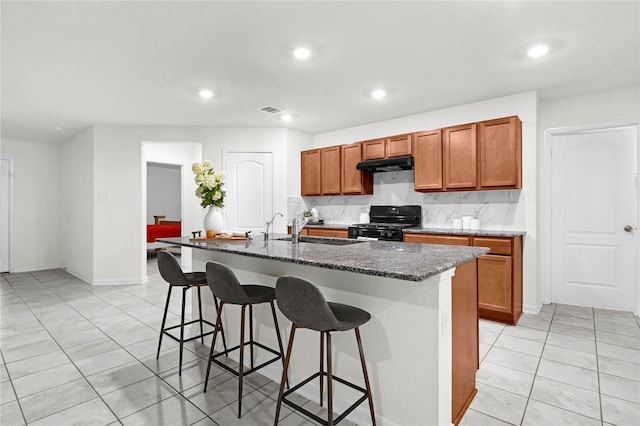 11642 Bodark Valley Ln, Houston, TX 77038 - kitchen featuring black range, under cabinet range hood, light tile patterned floors, a kitchen bar, and decorative backsplash