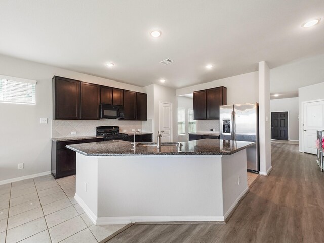 12519 Crathie Dr, Humble, TX 77346 - kitchen with black appliances, dark brown cabinets, a center island with sink, dark stone countertops, and recessed lighting