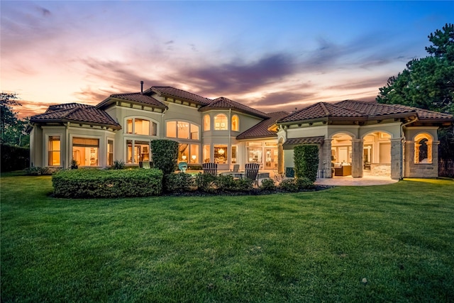 27 S Glenwild Cir, The Woodlands, TX 77389 - back of property at dusk with a yard, stucco siding, a tile roof, and a patio area