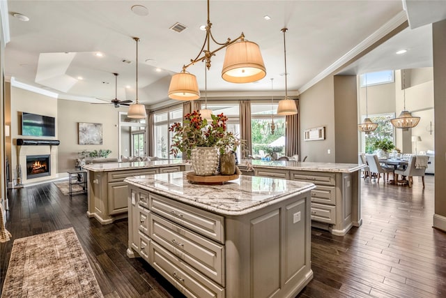 27 S Glenwild Cir, The Woodlands, TX 77389 - kitchen featuring a large island with sink, crown molding, a warm lit fireplace, open floor plan, and dark wood-style floors