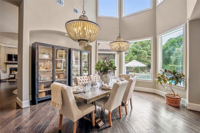 27 S Glenwild Cir, The Woodlands, TX 77389 - dining space featuring a chandelier, a towering ceiling, dark wood-type flooring, healthy amount of natural light, and a lit fireplace