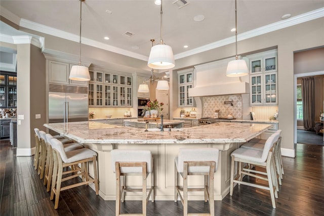 27 S Glenwild Cir, The Woodlands, TX 77389 - kitchen featuring built in appliances, a large island, dark wood-style flooring, backsplash, and premium range hood