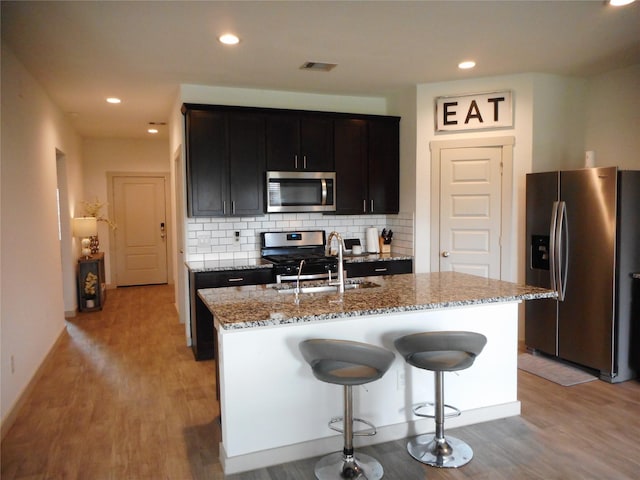 8227 Precious Passing Way, Rosharon, TX 77583 - kitchen with stainless steel appliances, light stone counters, light wood-style flooring, tasteful backsplash, and a center island with sink