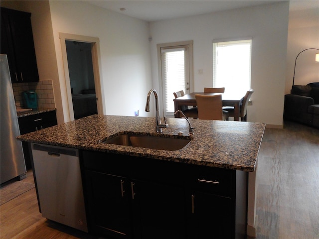 8227 Precious Passing Way, Rosharon, TX 77583 - kitchen featuring stainless steel appliances, an island with sink, dark cabinets, wood finished floors, and dark stone counters