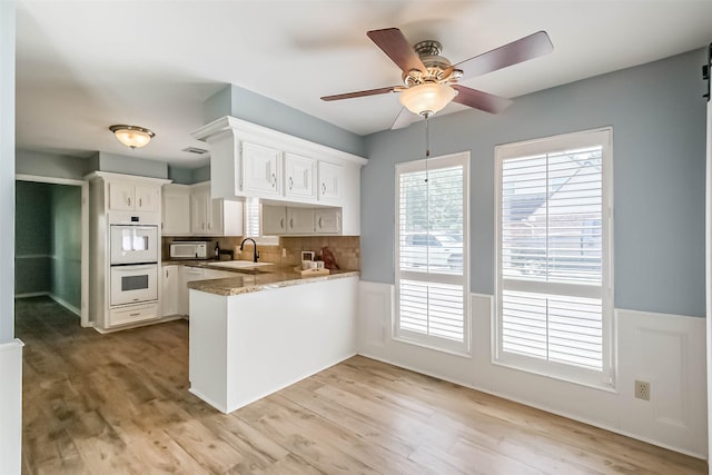 1711 Earl Of Dunmore St, Katy, TX 77449 - kitchen featuring white appliances, a peninsula, white cabinetry, light wood finished floors, and a wainscoted wall