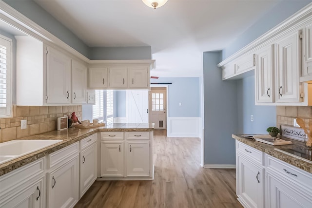1711 Earl Of Dunmore St, Katy, TX 77449 - kitchen featuring white cabinetry, wainscoting, light wood finished floors, a peninsula, and backsplash