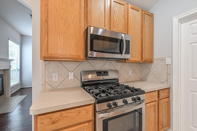 1518 Bugle Run Dr, Katy, TX 77449 - kitchen with appliances with stainless steel finishes, light countertops, decorative backsplash, dark wood-style flooring, and a tiled fireplace
