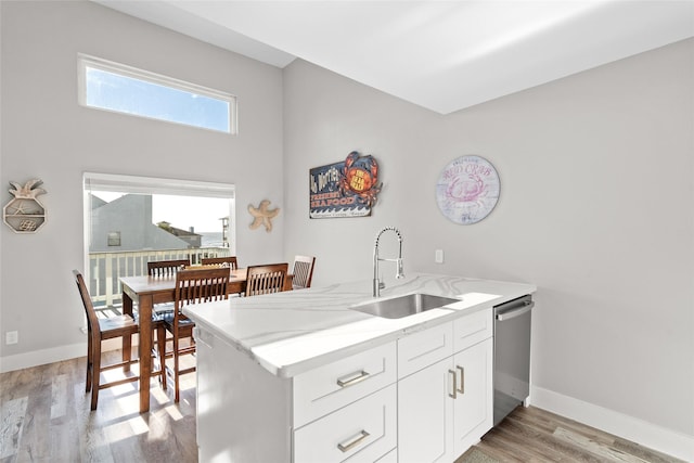 17711 Termini San Luis Pass Rd, Galveston, TX 77554 - kitchen with stainless steel dishwasher, light wood finished floors, white cabinetry, light stone counters, and a peninsula