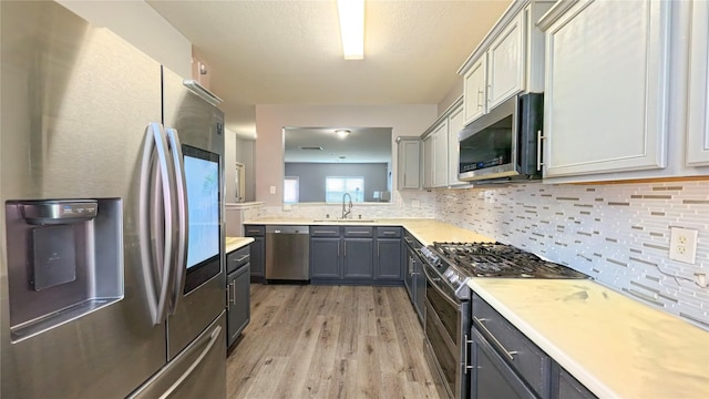1855 Garnet Breeze Dr, Rosharon, TX 77583 - kitchen with stainless steel appliances, light countertops, light wood-type flooring, decorative backsplash, and gray cabinets