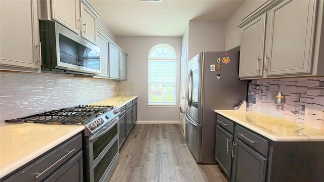 1855 Garnet Breeze Dr, Rosharon, TX 77583 - kitchen with appliances with stainless steel finishes, light wood-type flooring, light countertops, decorative backsplash, and gray cabinets