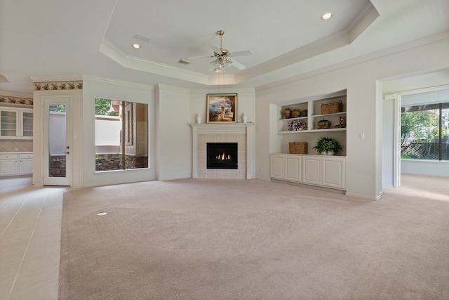 102 W Racing Cloud Ct, The Woodlands, TX 77381 - unfurnished living room featuring crown molding, a raised ceiling, a ceiling fan, a tile fireplace, and light colored carpet